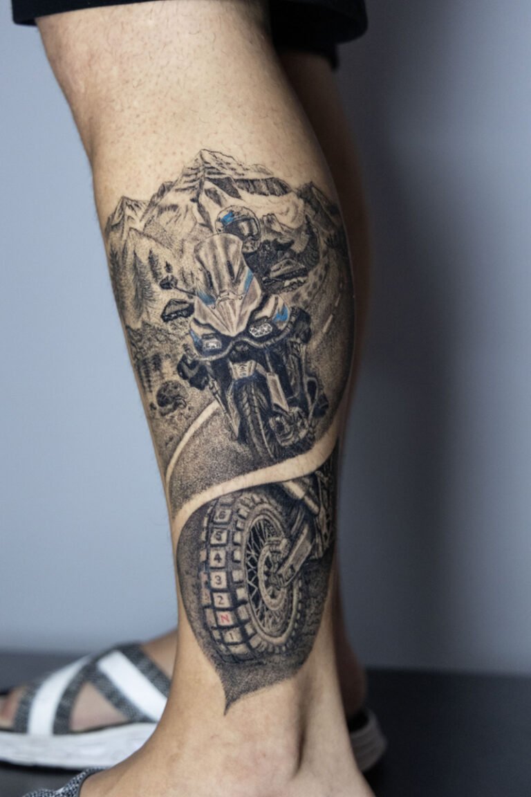 Tatuaje realista de moto trail y paisaje de montaña en la pierna, por Paco Serra – Museum Tattoo Valencia