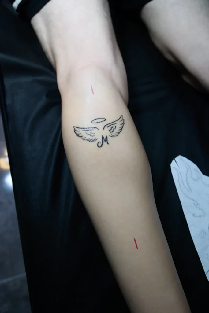 Antes del cover up: pequeño tatuaje de alas con aureola en la pierna, marcado para el nuevo diseño